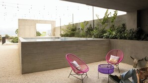 A modern outdoor pool area with concrete walls, two pink and one purple wicker chair, and a bull's head sculpture. - Catorce Urbano (San José)