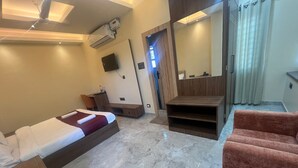 A hotel room with a bed, a seating area with a sofa, a small table, a TV mounted on the wall, and a mirror.
