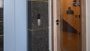 Um elevador moderno com painel digital, parede de mármore e porta de madeira.