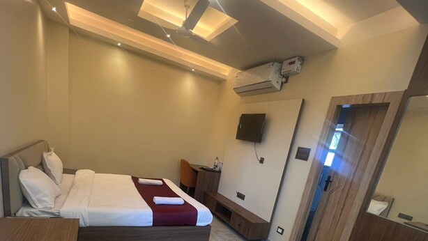 Quarto de hotel moderno com uma cama, uma escrivaninha, uma cadeira, uma televisão e um espelho.