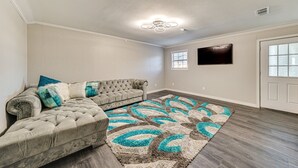 A spacious living room with a tufted sofa, a patterned rug, and a flat-screen TV mounted on the wall.