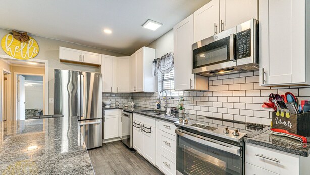 A modern kitchen with white cabinets, stainless steel appliances, and a granite countertop.