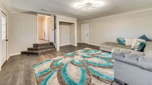 A spacious living room with a grey sofa, a patterned rug, and a staircase leading to another room.