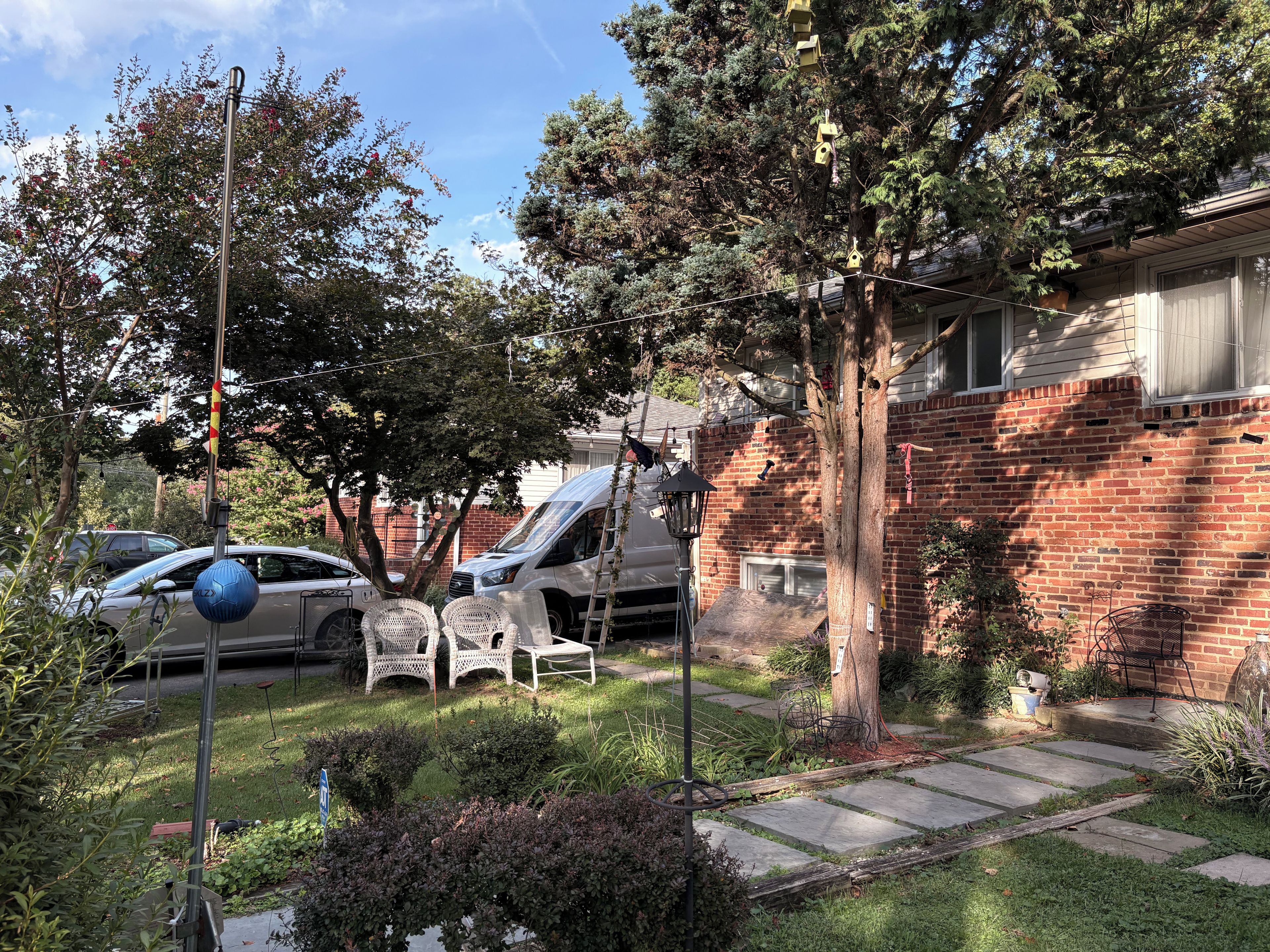 A residential area with a brick house, parked cars, and a garden with a lawn and pathway.