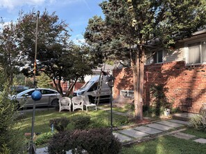 A residential area with a brick house, parked cars, and a garden with a lawn and pathway. - Hummingbird nest suite in Silver Spring, MD (Silver Spring)