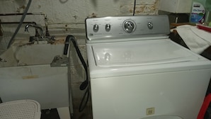 Een witte wasmachine met bedieningsknoppen, een rode emmer en een witte plastic bak.