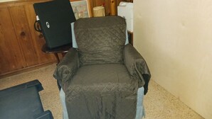 Une pièce comprenant un fauteuil capitonné, une petite table avec un ordinateur portable et un tableau encadré accroché au mur.