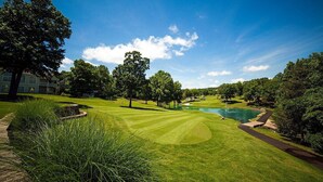 A well-maintained golf course with a pond, surrounded by trees and a building in the background. - Indoor Pool-Central Branson (Branson)
