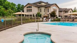 A swimming pool with a unique shape, surrounded by a fence and a building with multiple windows. - Indoor Pool-Central Branson (Branson)