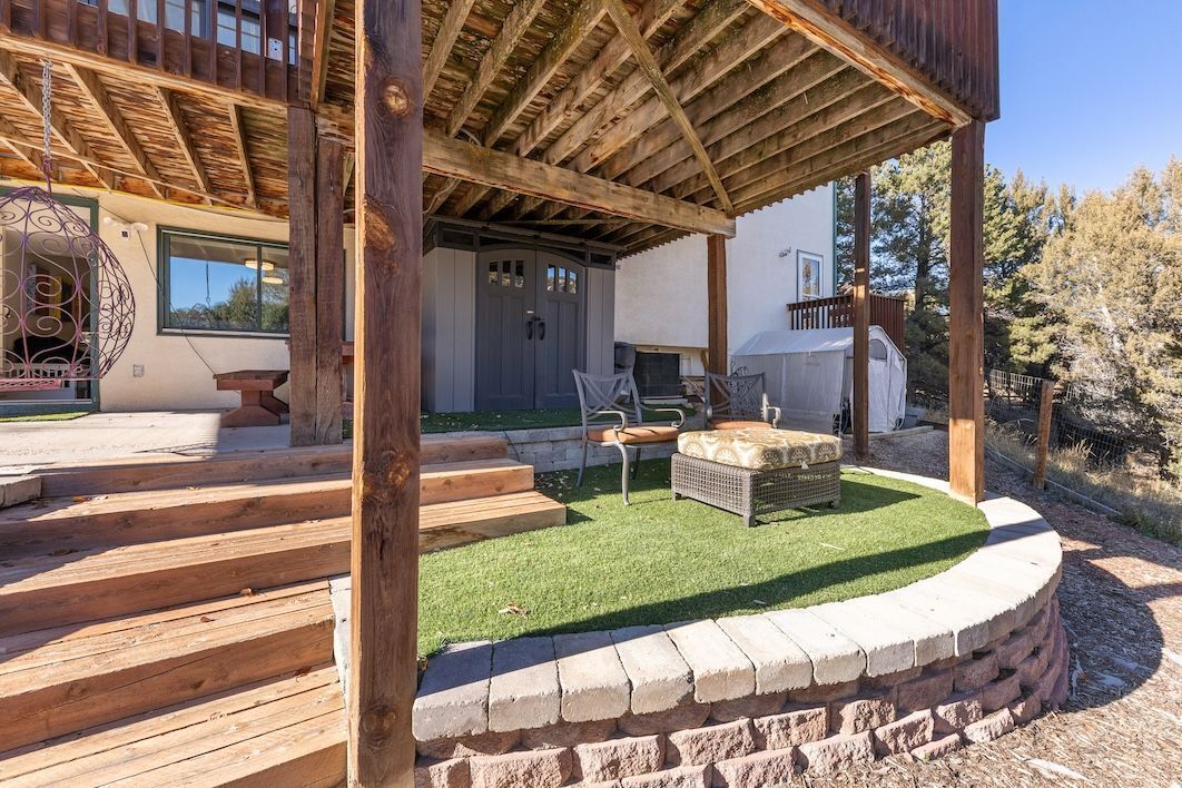 Een overdekt buitengebied met houten trappen, een zithoek met een tafel en stoelen, en een barbecue.