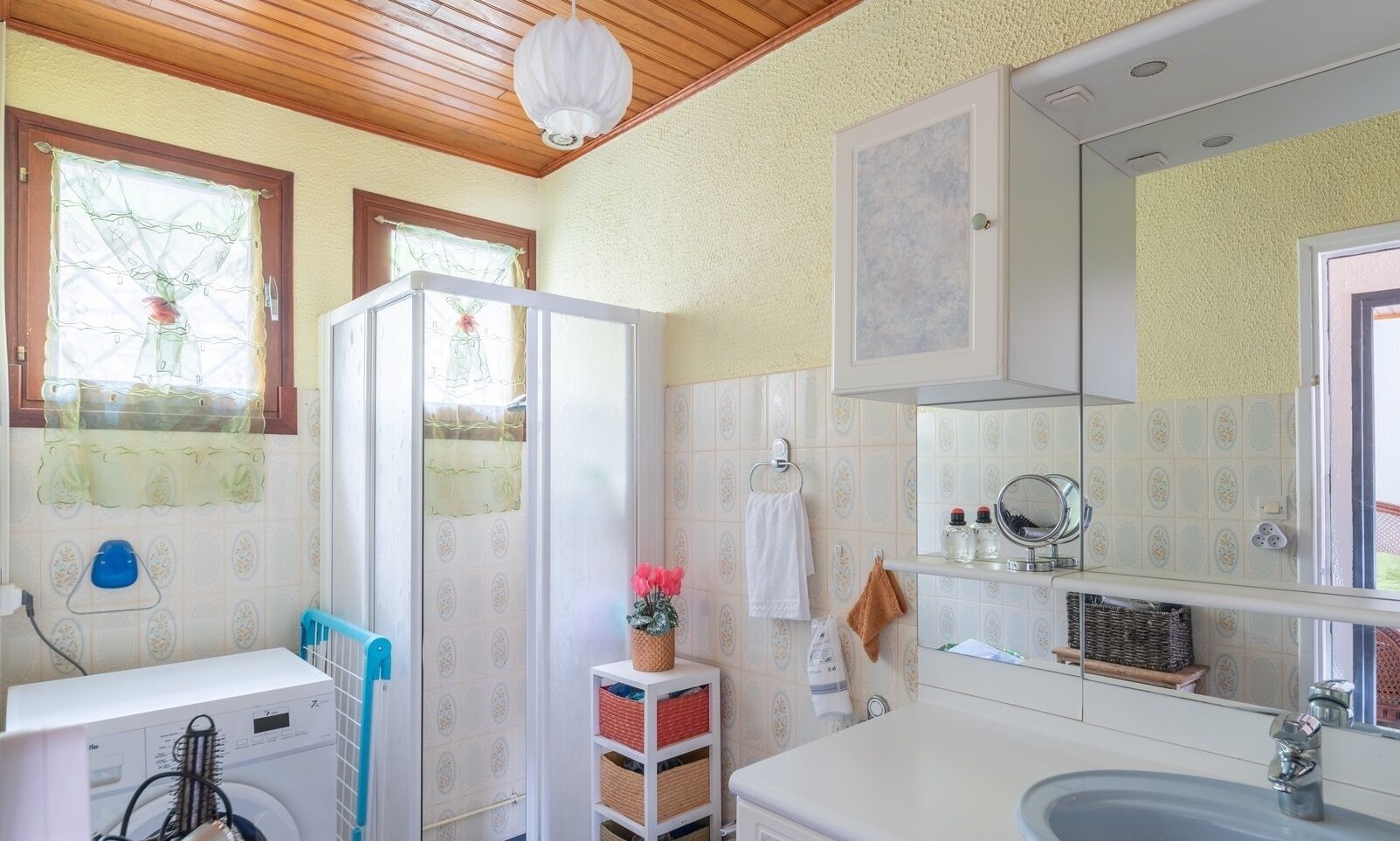 Une salle de bain équipée d’un lave-linge, d’un lavabo, d’un miroir et d’un porte-serviettes.