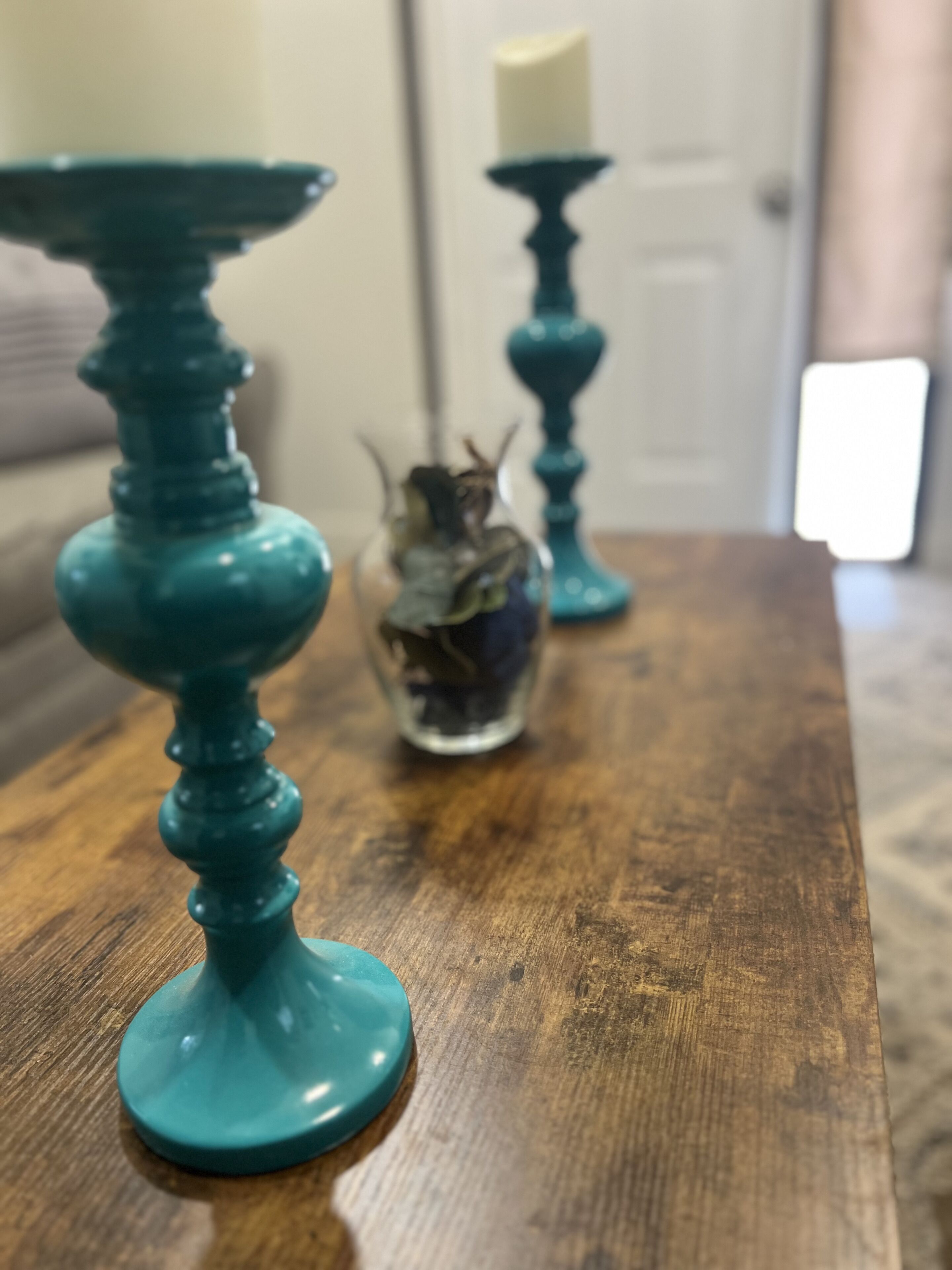 A wooden table with teal candle holders and a glass vase with dried flowers.