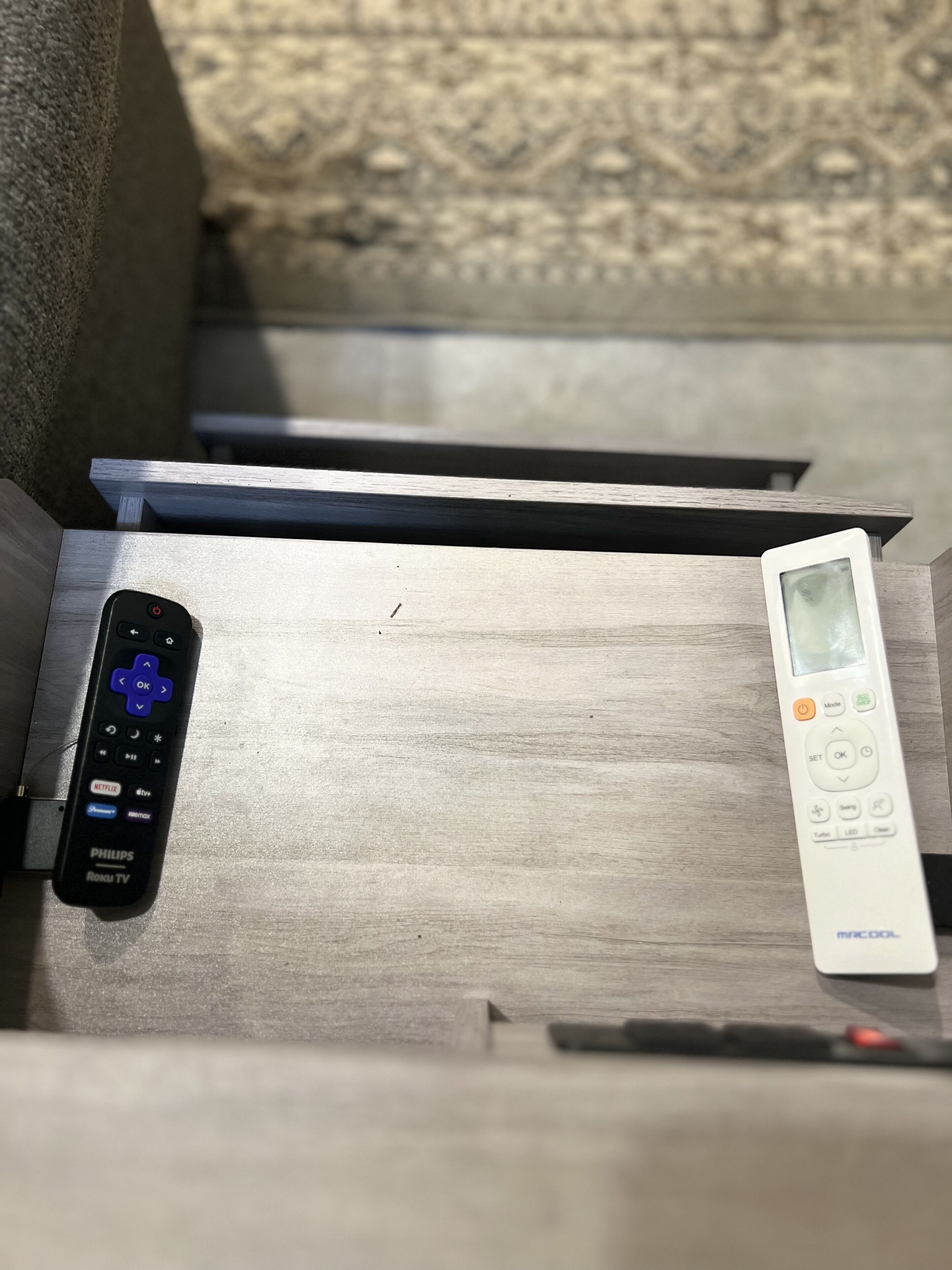 A wooden bench with two remote controls placed on it.