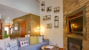 Een gezellige woonkamer met een stenen openhaard, een grijze bank en een ronde salontafel.