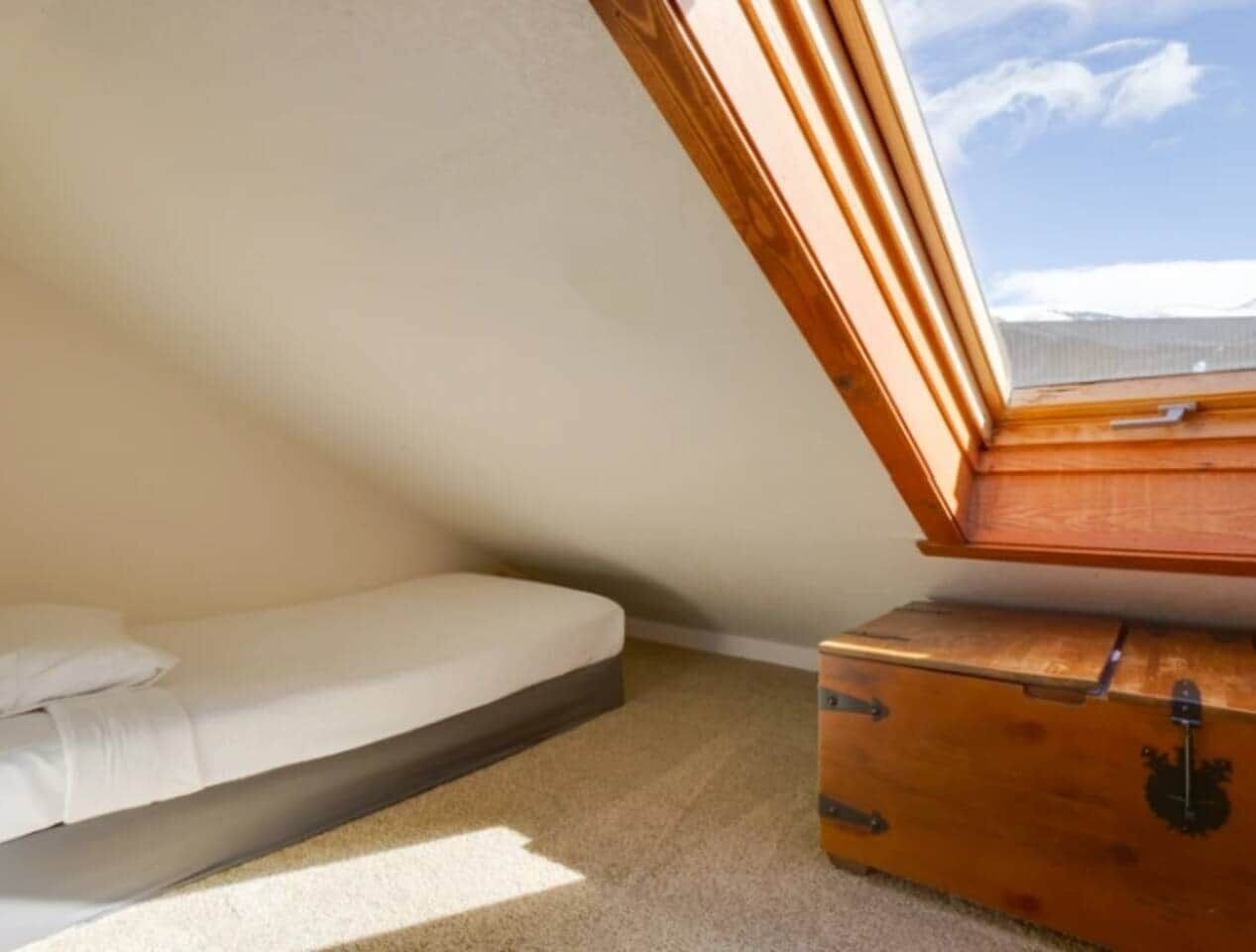 A small, single-room attic bedroom with a slanted ceiling, a wooden chest, and a bed.