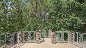 Een stenen brug met metalen hekwerk, omringd door weelderige groene begroeiing.