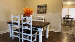 Een eethoek met een donker houten tafel en witte stoelen, een vaas met oranje bloemen en een ingelijste foto aan de muur.