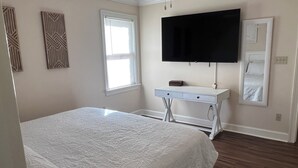 Een slaapkamer met een bed, een witte dressoir, een televisie en een raam.