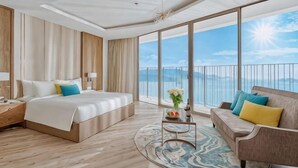 Ein Hotelzimmer mit einem großen Bett, einer Couch, einem Couchtisch und Blick aufs Meer.