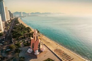 A coastal cityscape with a prominent pink building near the beach, a clear view of the sea, and a road running parallel to the waterfront. - Panorama Nha Trang SanVilla (Nha Trang)