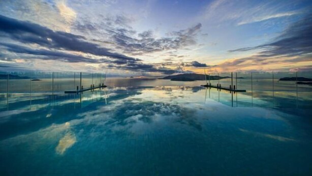 Ein großer, klarer Pool mit Glasboden, umgeben von einer Glaskonstruktion und Blick auf den Sonnenuntergang.