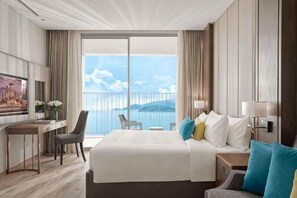 A hotel room with a large bed, a desk, a chair, a TV, and a balcony with a view of the sea. - Panorama Nha Trang SanVilla (Nha Trang)