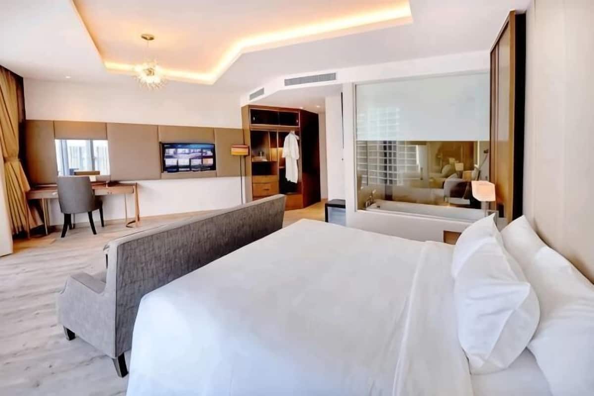 Une chambre d’hôtel avec un grand lit, un bureau, une télévision et une salle de bain avec un miroir.
