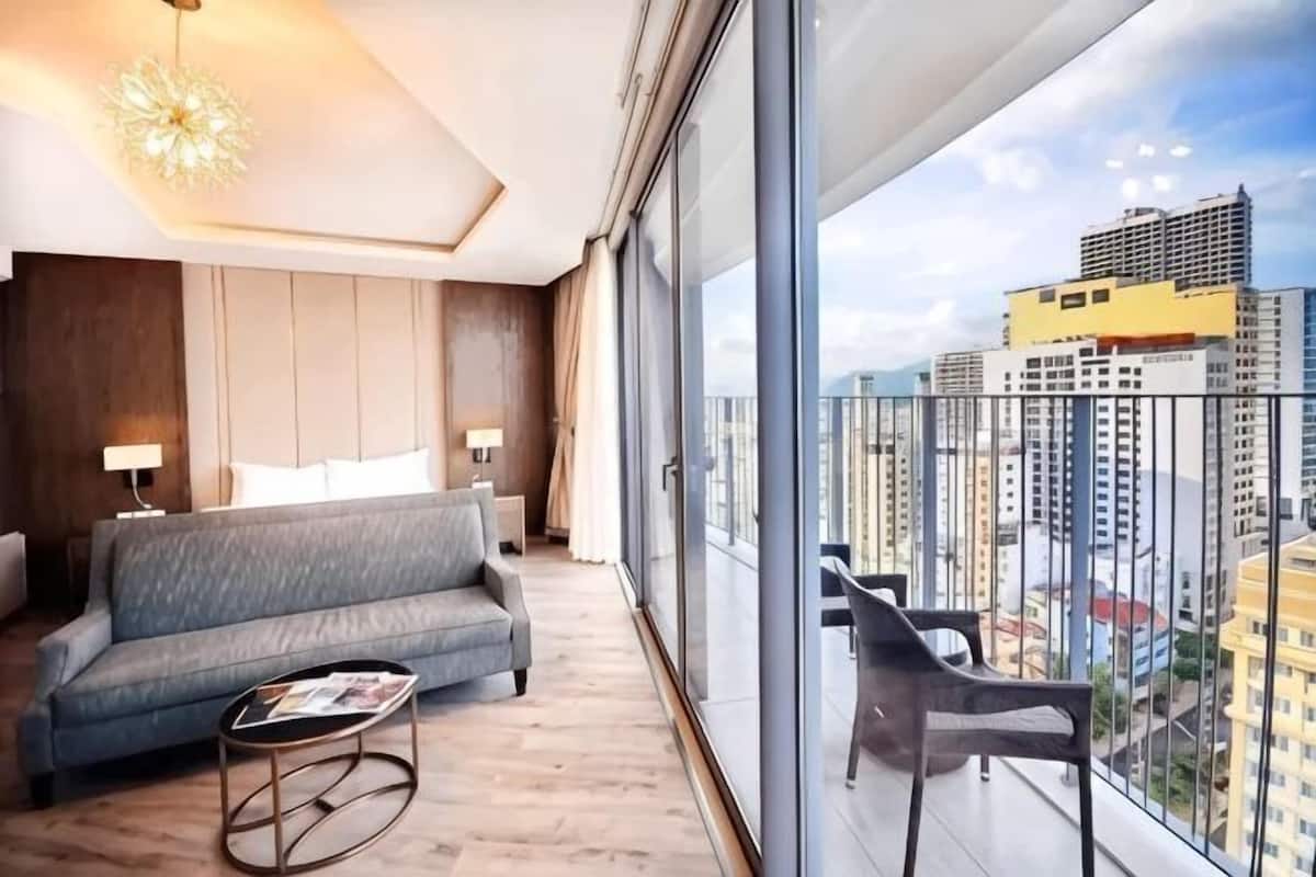 Une chambre d’hôtel moderne dotée d’un grand balcon, d’un canapé, d’une table basse et offrant une vue sur le paysage urbain.