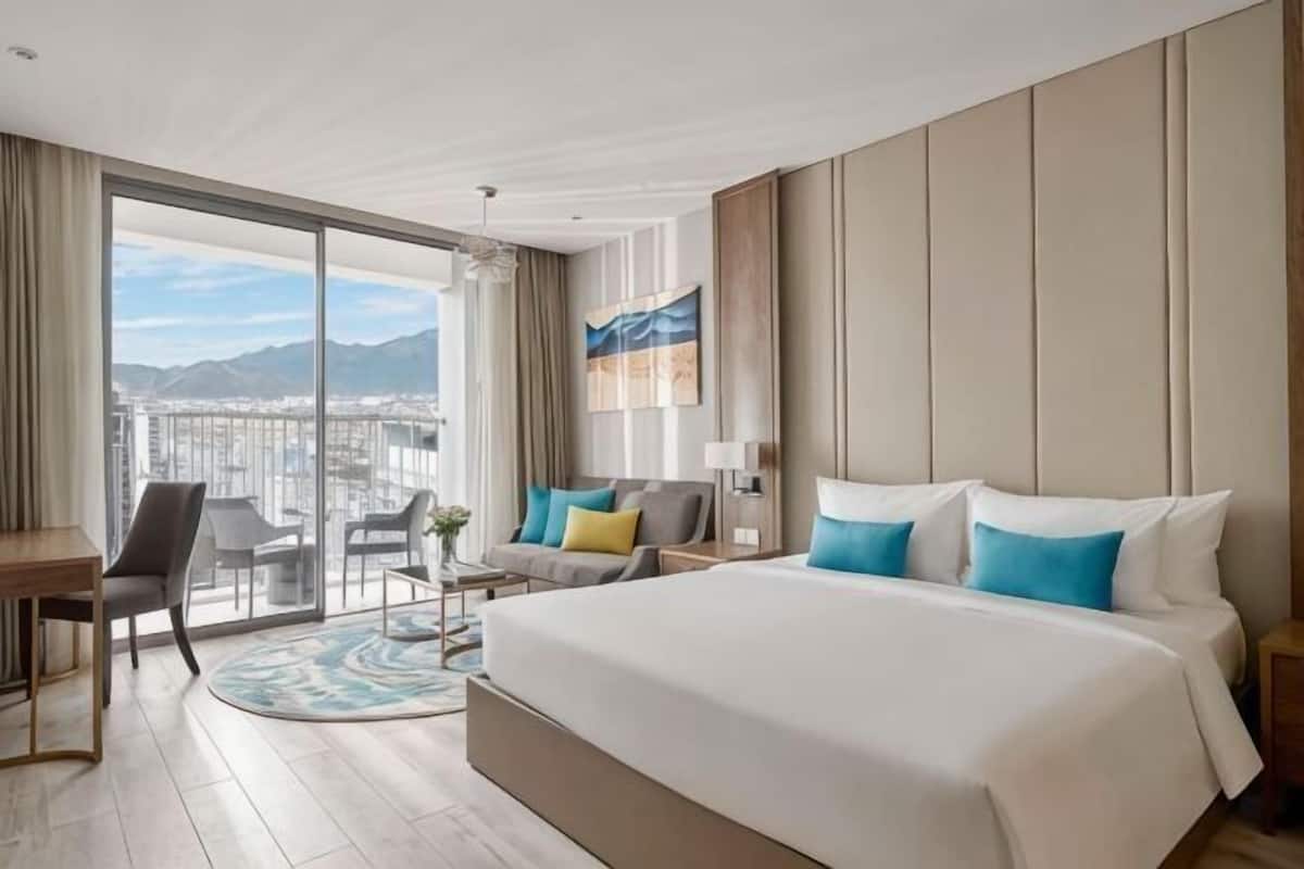Une chambre d’hôtel avec un grand lit, un bureau, une chaise, un canapé et un balcon offrant une vue sur la ville.