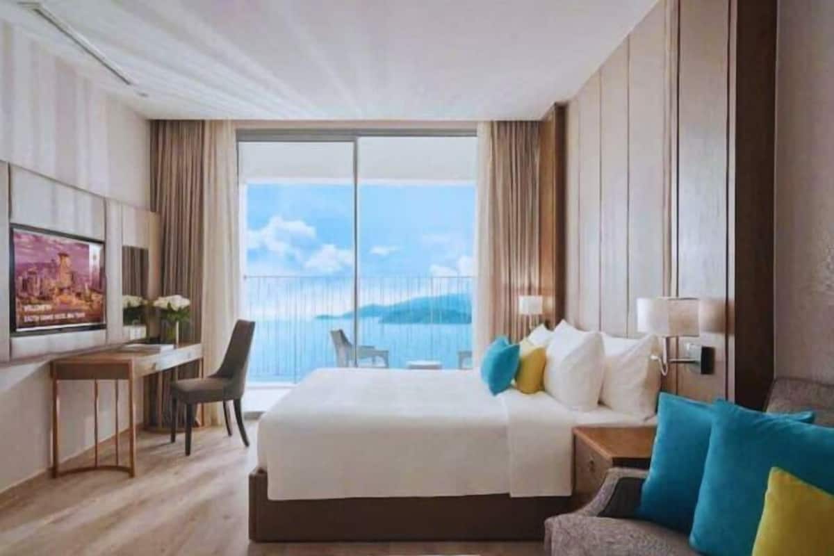 Une chambre d’hôtel avec un grand lit, un bureau et une chaise. Une grande fenêtre offre une vue sur la mer.