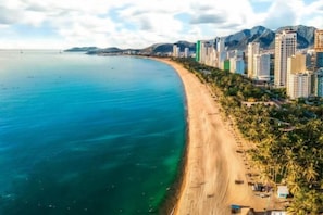 Vista aérea de una ciudad costera con una playa de arena extensa, edificios altos y montañas al fondo.