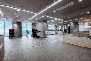 Een moderne fitnessruimte met trainingsapparatuur, een receptiebalie en grote ramen met uitzicht.