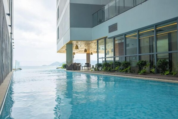 A swimming pool adjacent to a modern building with large windows and outdoor seating. - Panorama Nha Trang SanVilla (Nha Trang)