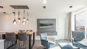 A modern dining area with a wooden table, grey upholstered chairs, and hanging pendant lights. - Luxusapartement mit Meerblick (Nordstrand)