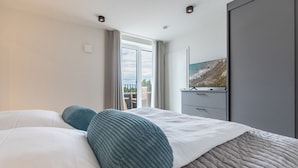 A hotel room with a large bed, a flat-screen TV on a dresser, and a balcony with a view. - Luxusapartement mit Meerblick (Nordstrand)