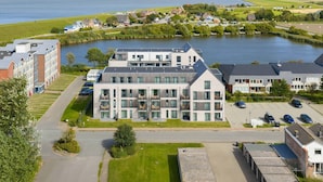 A modern building with multiple floors, a parking lot, and a view of a lake. - Luxusapartement mit Meerblick (Nordstrand)