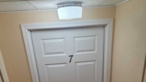 Une porte blanche portant le numéro 7, un mur beige à la texture particulière et un plafond à motifs.