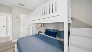 A bedroom with a bunk bed, a small bedside table, a wall-mounted shelf, and a door. - Sea Breeze Hideaway (Panama City Beach)
