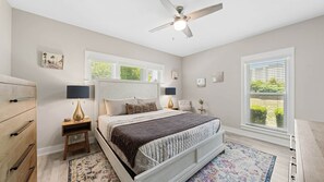 Une chambre à coucher avec un lit, des tables de chevet, un ventilateur de plafond et une fenêtre avec des stores.