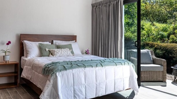 A bedroom with a large bed, a nightstand, a potted plant, and a view of greenery through a sliding glass door. - Where the Forest Meets Serenity (Monteverde)