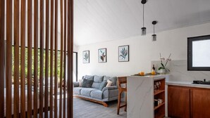 A modern kitchen with a marble countertop, wooden cabinets, and a grey sofa in the living area. - Where the Forest Meets Serenity (Monteverde)
