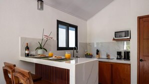 Eine kleine Küche mit weißem Marmor-Arbeitsplatz, Holzstühlen, einem Esstisch, einer Mikrowelle und einem Fenster.