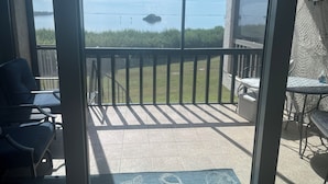Eine überdachte Terrasse mit Blick auf ein Gewässer, eine kleine Insel und eine Rasenfläche.