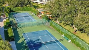 Ein Tennisplatz mit grüner Belag, umgeben von Bäumen und einem Zaun.