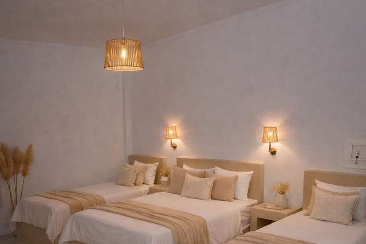 A bedroom with two beds, a hanging light fixture, wall sconces, and a woven rug.