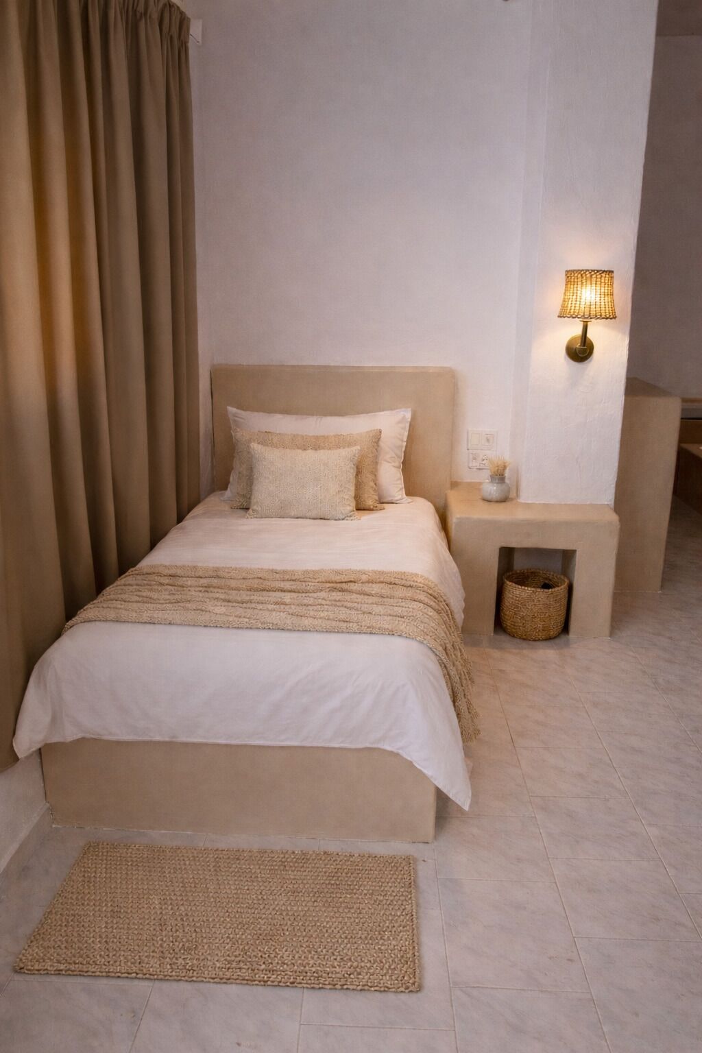 A bedroom with a bed, bedside table, lamp, and a woven mat.