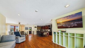 Amplia sala de estar con piso de madera, comedor y cocina.