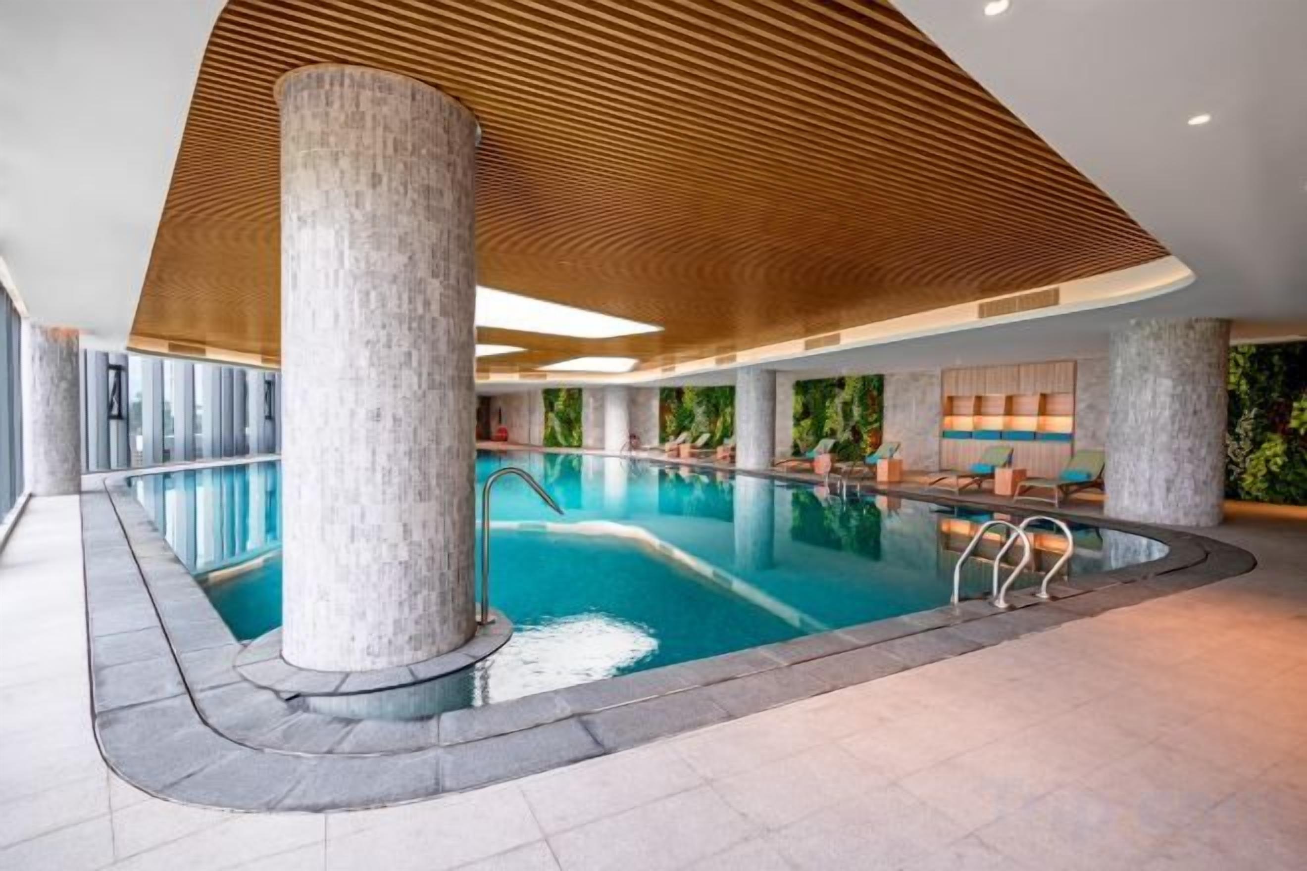 Modernilla designilla varustettu sisäuima-allas, jossa on puinen katto ja kivipylväät.
