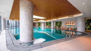 Ein Hallenbad mit modernem Design, das sich durch eine Holzbalkendecke und Steinsäulen auszeichnet.
