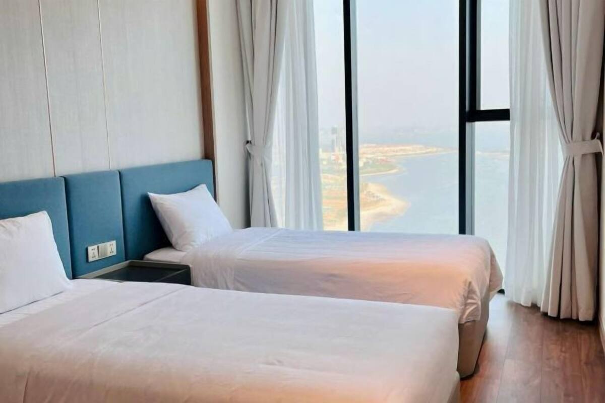 Een hotelkamer met twee bedden, uitzicht op een waterpartij en een groot raam met gordijnen.